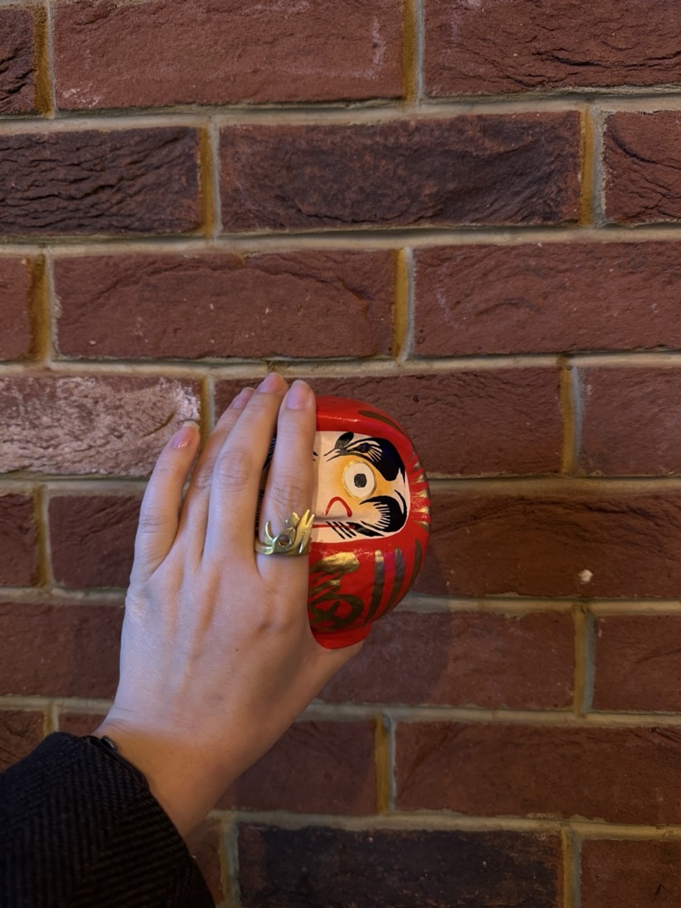 A daruma doll held against the cafe's brick wall
